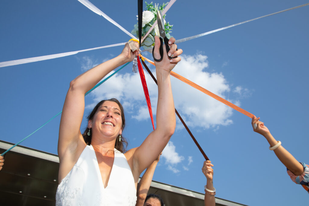 Mariée souriante lors du jeu des rubans avec ses invitées en plein air, photographe Gironde.
