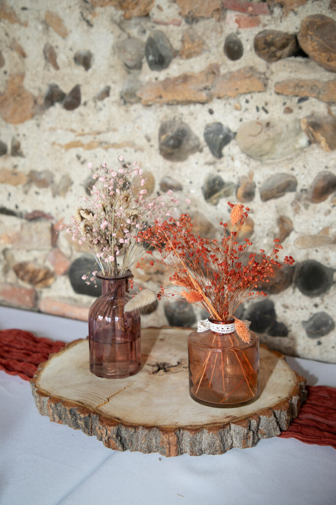 Décoration de table de mariage bohème avec fleurs séchées dans des vases ambrés sur un socle en bois, Gironde.