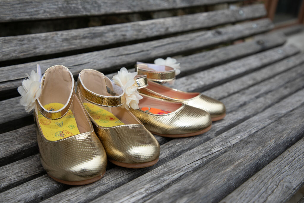 Chaussures dorées d'enfants d'honneur sur un banc en bois, mariage en extérieur dans le Médoc.