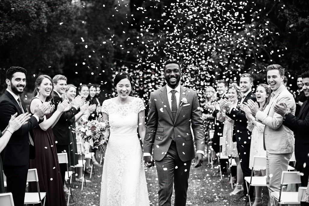 Sortie de cérémonie de mariage joyeuse sous une pluie de pétales, photographe mariage Bordeaux.