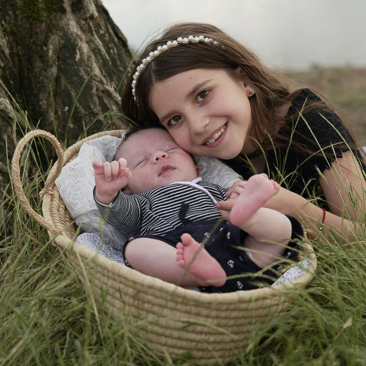 Nouveau-né endormi paisiblement dans un panier en osier entouré de fleurs, séance photo naissance à domicile.